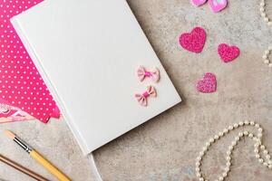 A collection of crafting materials arranged on a textured surface with a blank notebook, decorative paper, and various embellishments photo