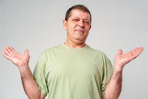 A middle-aged man with a neutral expression raises his hands in a questioning gesture against a plain backdrop photo