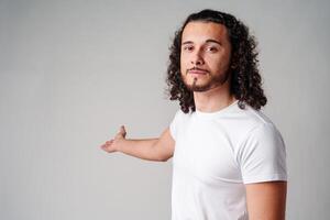 Young man in a white t-shirt and jeans pointing confidently while smiling in a studio setting photo
