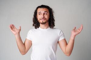 A man with curly hair expressing uncertainty while standing against a neutral background photo