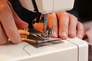 Hands sewing fabric using a sewing machine on a wooden table in a well-lit workspace photo