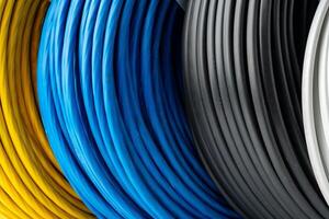 Four Spools of Electrical Wire in Yellow, Blue, Black, and White Colors. A Close-Up Photo of Four Spools of Electrical Wire, Each Wound in a Different Color.