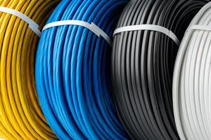 Four Spools of Electrical Wire in Yellow, Blue, Black, and White Colors. A Close-Up Photo of Four Spools of Electrical Wire, Each Wound in a Different Color.
