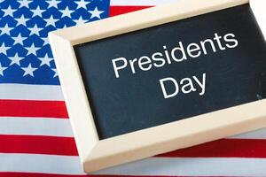 the text happy presidents day written in a chalkboard and a flag of the United States photo