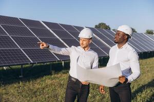Engineers Collaborating at a Solar Power Plant with Blueprints in Hand Under a Clear Sky photo