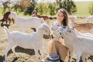 Young Woman Enjoys Peaceful Moment with Friendly Goats in Sunny Pasture on Farm, Experiencing Joy and Harmony Amidst Nature and Lovable Animals, Creating a Heartwarming Rural Encounter with Farm Life photo