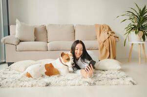 Portrait of beautiful young woman with her dog using mobile phone at home photo