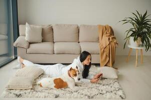 Portrait of beautiful young woman with her dog using mobile phone at home photo