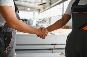 Two engineers in hard hats shake hands in a factory. photo