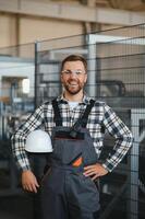 Smiling and happy employee. Portrait of industrial worker indoors in factory. Young technician with white hard hat photo