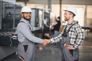 Two engineers in hard hats shake hands in a factory. photo
