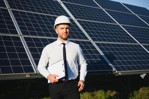 Man in business suit, solar panels on backstage. Client in white helmet standing at solar energy power station photo