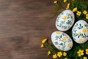 Hand-painted Easter eggs adorned with floral patterns on a rustic wooden table along with yellow flowers and green moss photo
