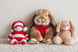 A fluffy rabbit in a festive holiday outfit sits beside soft toys on a light carpet in a cozy setting photo