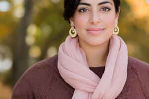 A woman in cozy fall fashion with a blush scarf and knit sweater amid a beautiful autumn forest background photo