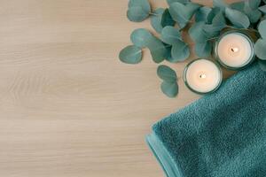 Tranquil spa setting with teal towels, eucalyptus branches, and lit candles on natural wood surface for relaxation photo