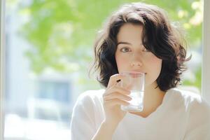 Young woman enjoying a glass of water while sitting by a sunlit window in a minimalist setting photo
