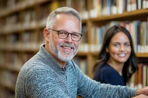 Middle-aged man smiling at the camera while reading in a library with a young woman in the background photo