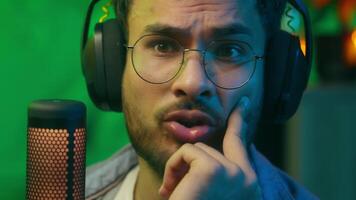 Emotional talking in mic radio host gamer streamer night game addict at home looking at computer screen Indian Caucasian man male guy in headphones talk at microphone speaking internet online stream video