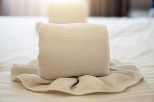 Two white towels neatly folded and arranged on a bed. One towel is rolled up and placed vertically. Arrangement is a common way to present towels in hotel rooms. photo