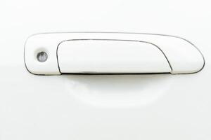 View of a used white car door handle. handle itself is a rectangular shape with a slight curve at the bottom. Round hole at the top end of the handle likely for a keyhole. Stains in the keyhole. photo