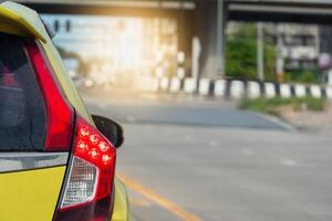 Rear side of alone yellow car with turn on brake light on the road. Backgound blurrd of bridge and traffice light. photo