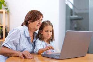 Granddaughter and grandmother using laptop together on table at home photo