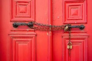 Closeup of metallic chains and locks in handles on red closed doors photo