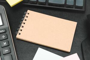 Top view of notebook. Blank paper notepad on office desk table with keyboard and other supplies. Blank notebook page for input the text. copy space, flat lay. photo