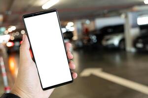 Mockup blank screen mobile phone for app or web site mockup. Smart phone with white screen in hand on Blur car parking background. photo
