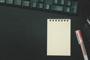 Top view of notebook. Blank paper notepad on office desk table with keyboard and other supplies. Blank notebook page for input the text. copy space, flat lay. photo