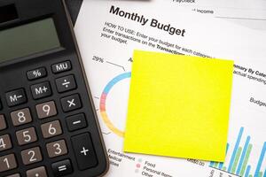 Blank Sticky note with calculator on desk with monthly budget graph. Financial data analyzing. Working on desk with using calculator, finance accounting. Copy space. photo