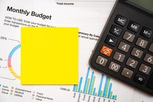 Blank Sticky note with calculator on desk with monthly budget graph. Financial data analyzing. Working on desk with using calculator, finance accounting. Copy space. photo