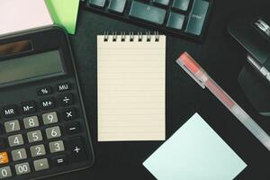 Top view of notebook. Blank paper notepad on office desk table with keyboard and other supplies. Blank notebook page for input the text. copy space, flat lay. photo