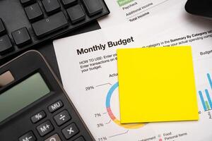 Blank Sticky note with calculator on desk with monthly budget graph. Financial data analyzing. Working on desk with using calculator, finance accounting. Copy space. photo