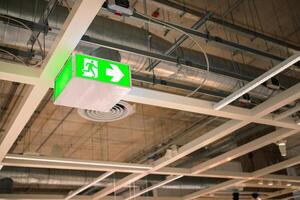Selective fire exit sign on ceiling. Green fire escape sign hang on the ceiling. Green emergency exit sign showing the way to escape.Fire exit in the building. photo