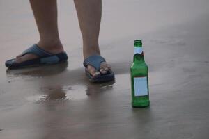 A womans leg and a beer bottle, positioned on a sandy beach by the ocean photo