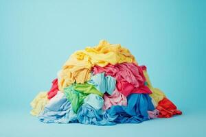 A vibrant and colorful heap of crumpled laundry in a multitude of shades rests against a soft blue backdrop, elegantly showcasing the delightful chaos that comes with everyday cleaning chores photo