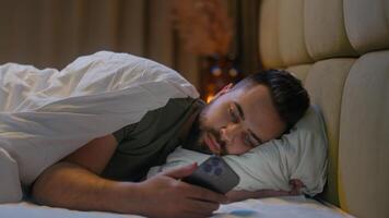 Caucasian man lying in bed bedroom user mobile phone smartphone cellphone gadget technology male guy connected scrolling website browsing network cyber ecommerce chatting internet distance communicate photo