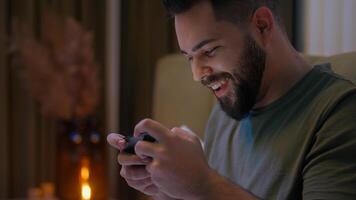 Excited Caucasian man playing mobile phone smartphone cellphone game gamer control emotional male guy tense home pastime gadget technology addicted stuck competition leisure player online tournament photo