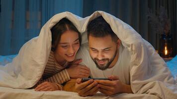contento novio Novia funda Nordica cobija hogar juntos Pareja hombre mujer acecho móvil teléfono teléfono inteligente en línea social redes dormitorio Noche hojeada cómodo ciberespacio web hembra masculino foto