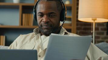 African american man teacher businessman freelancer in headset checking documents entering data in laptop remote working at home using computer application paying bills processing online information photo