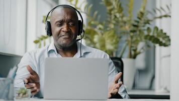 Senior african instructor teacher wears headphones using web camera for communication with clients teaching online consultation during coronavirus pandemic calling remote by computer in office photo