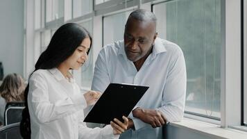 Diverse african and arabian colleagues multiracial people business partners stand near window discussing paper graphics strategic plans reading documents in tablet folder for paperwork documentation photo