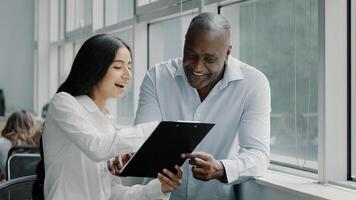 Diverse african and arabian colleagues multiracial people business partners stand near window discussing paper graphics strategic plans reading documents in tablet folder for paperwork documentation photo