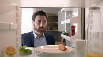 Hungry adult Caucasian businessman entrepreneur man after work open empty refrigerator with half lemon, lettuce leaf, bottle of milk and slice of bread eat crumbs POV point of view from inside fridge photo