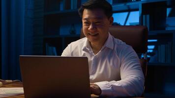 Middle-aged happy smiling businessman working with laptop and documents at dark night office Asian Korean man financial analyst accounting business using computer app at nighttime insomnia deadline photo