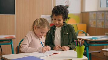 Talking African and Caucasian little school children multiracial diverse girl boy kids pupils schoolchildren together doing task exercise writing in copybook talk help learning class study education photo