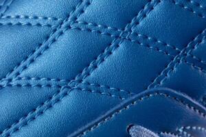 The macro texture of a blue leather sneaker with stitching. Part of the sports shoe is a close-up. photo