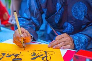 Vietnamese scholar writes calligraphy. Calligraphy festival is a popular tradition during Tet holiday. Writing couplets for Spring Festival, new year. photo